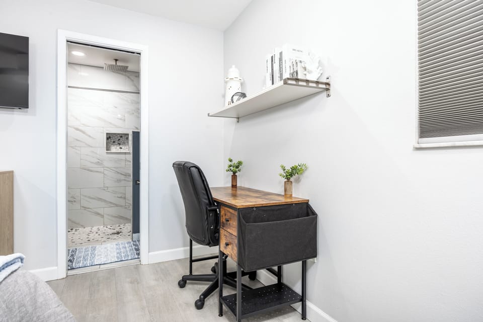 Your dedicated workspace awaits with a stylish desk, ergonomic chair, and natural light streaming through the window blinds.