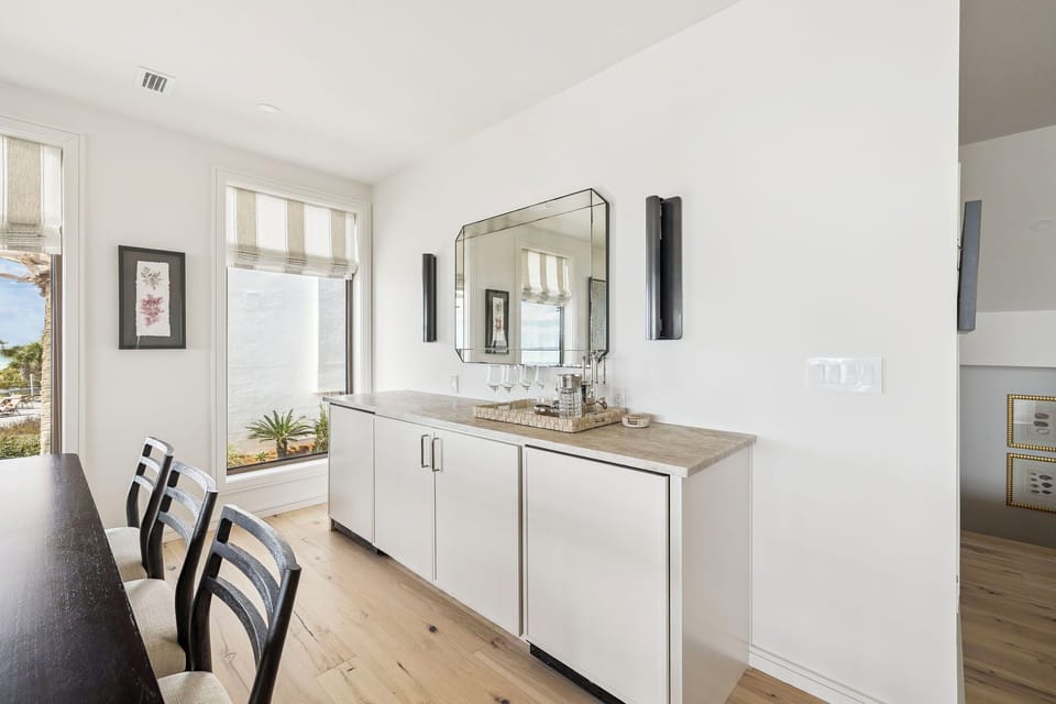 Sip morning coffee at your elegant dining space, where natural light streams through bamboo shades and sleek modern fixtures create a sophisticated coastal atmosphere.