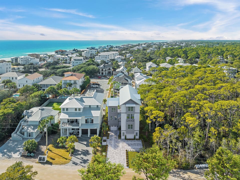 Aerial view showcasing a coastal community with modern homes nestled between pristine beaches and lush forest canopy.