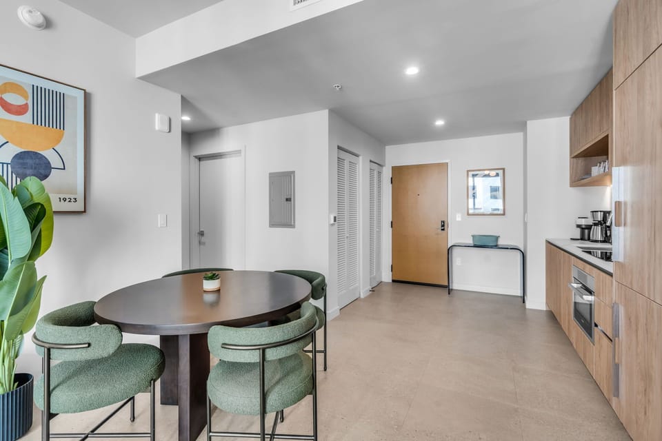This stylish dining area features a dark wood oval table paired with four modern, green upholstered chairs. The space is beautifully accented by minimalist wall art and a large leafy plant, creating a chic and inviting atmosphere for meals.