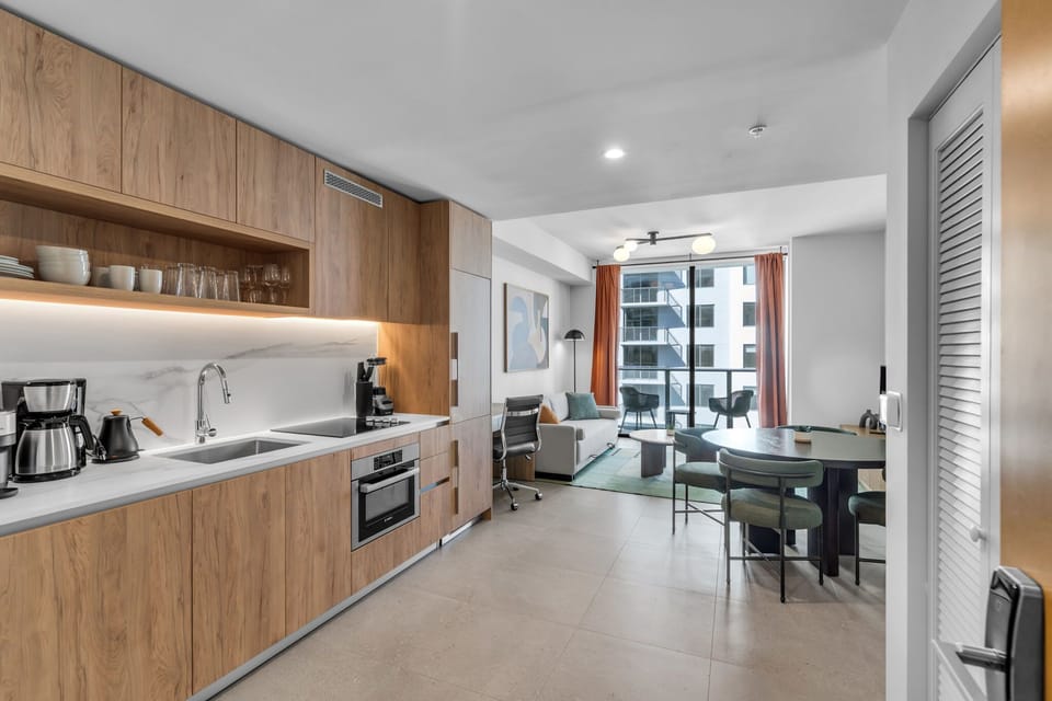 This sleek, modern kitchenette is designed for both style and function, featuring warm wood cabinetry and a marble-inspired backsplash. It comes fully equipped with premium integrated appliances, including a stovetop, oven, and a Nespresso machine :)