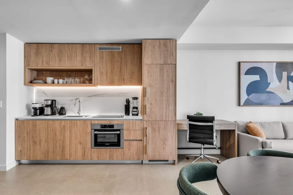 This sleek, modern kitchenette is designed for both style and function, featuring warm wood cabinetry and a marble-inspired backsplash. It comes fully equipped with premium integrated appliances, including a stovetop, oven, and a Nespresso machine :)