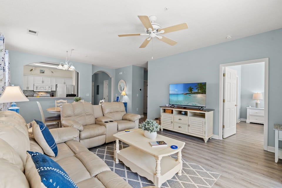 Bright coastal living room with recliners, smart TV, and open kitchen
