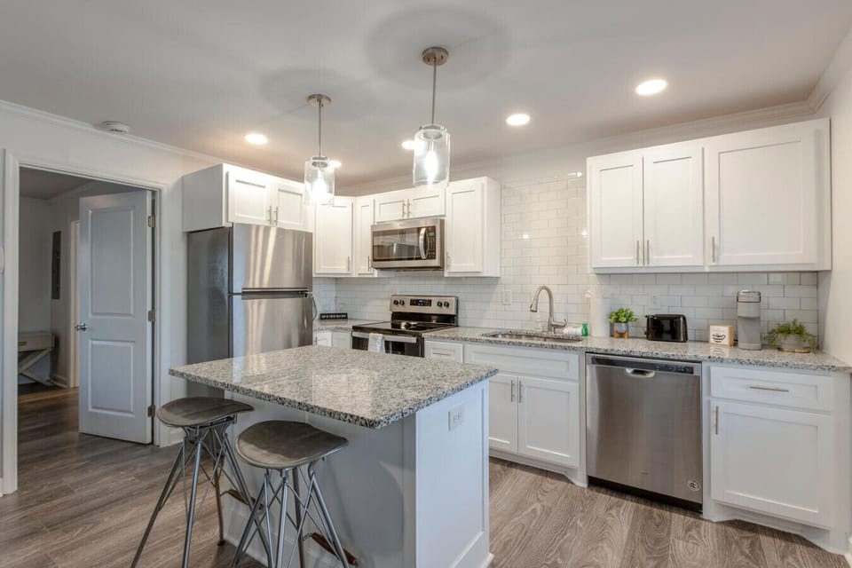 Kitchen with white cabinets, granite island with bar stools, pendant lights, and stainless steel appliances