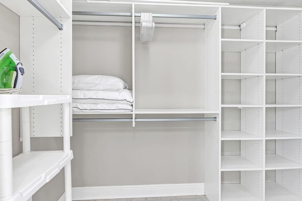Large master bedroom closet with tons of storage, extra pillows, iron and ironing board, pack n play, high chair, and folding card table and 4 chairs.