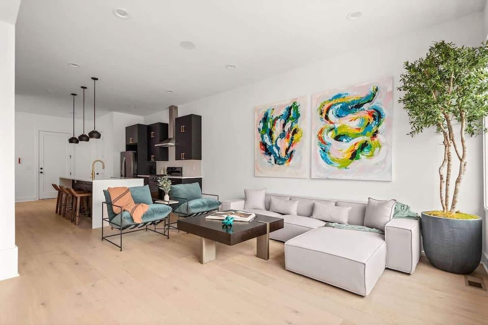 Bright and modern open concept living room with oversized windows, a comfortable sectional, bold artwork, and a Smart TV. (1st Floor)