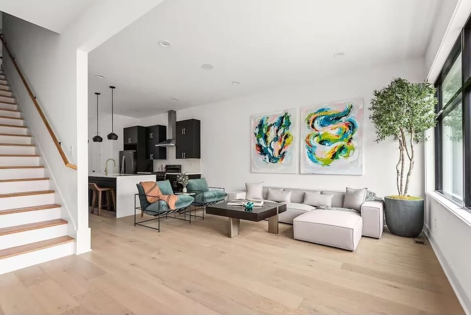 Bright and modern open concept living room with oversized windows, a comfortable sectional, bold artwork, and a Smart TV. (1st Floor)