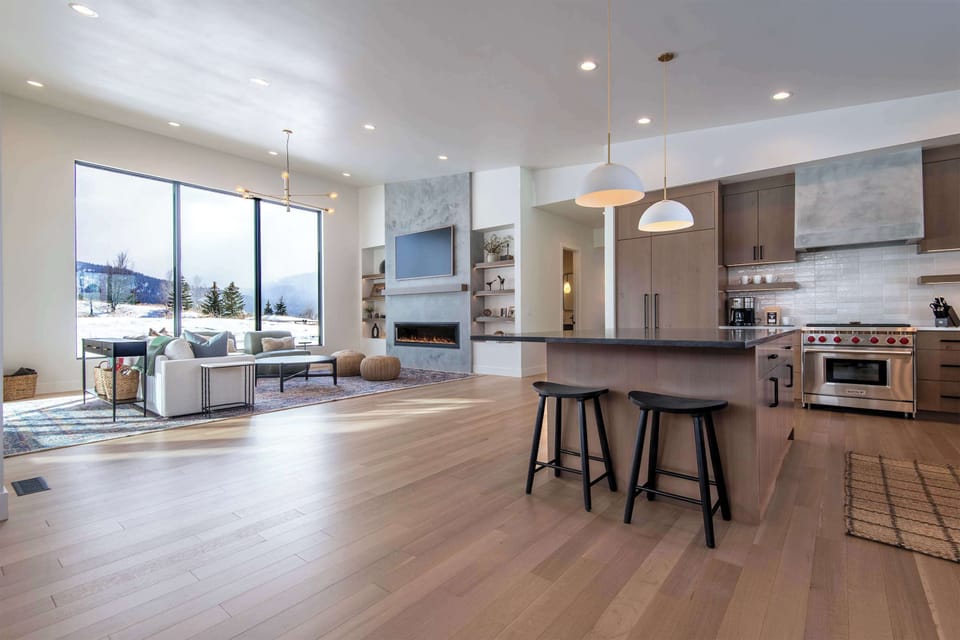 Showpiece kitchen with waterfall island, bar seating, and floor-to-ceiling Teton windows — cook breakfast while the mountains keep watch just outside the glass.