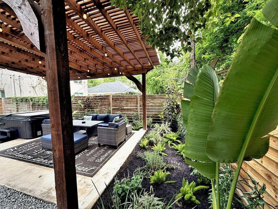 Fresh landscaping surrounds the covered pergola — green, private, and steps down the driveway.