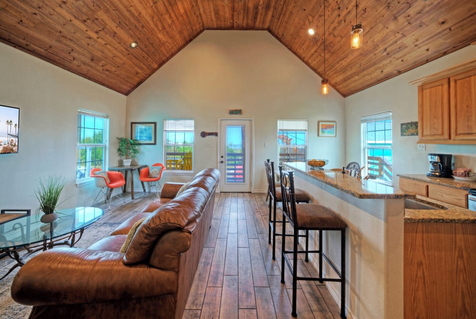 Bright open-concept great room with soaring wood ceilings, comfy seating, and a spacious kitchen bar for gathering.