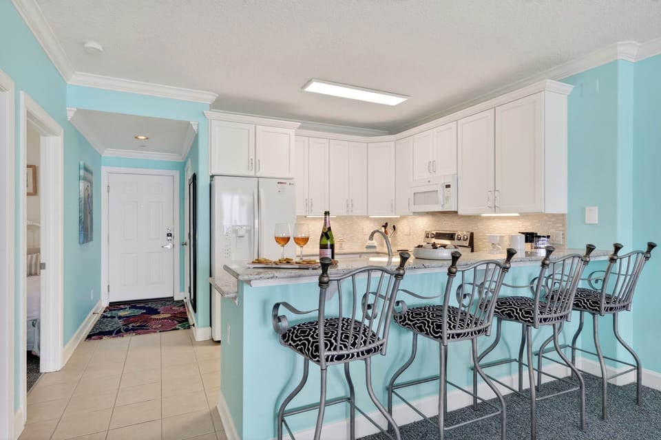 Bright coastal kitchen with bar seating—perfect for breakfast, snacks, and sunset happy hour at home.