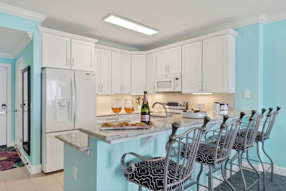 Bright coastal kitchen with bar seating—perfect for breakfast, snacks, and sunset happy hour at home.
