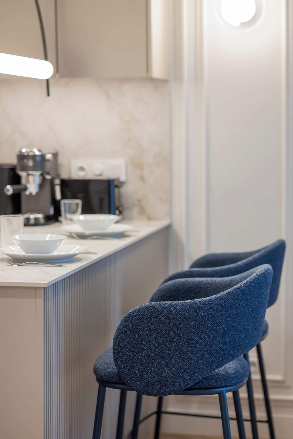 A close-up of a breakfast bar with a white countertop and two elegant navy blue bar chairs against a neutral wall backdrop.