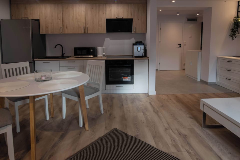 A compact kitchenette with light cabinet fronts and a wooden worktop. The equipment includes a cooktop, oven, and a coffee machine, suggesting the space is fully prepared for cooking.