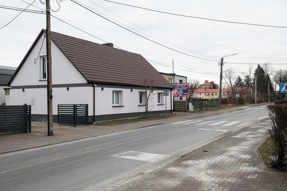 An exterior view of a white building with a traditional shape and a dark roof, located by the road. The property looks neat and well-maintained, with surroundings suggesting easy access to road infrastructure.