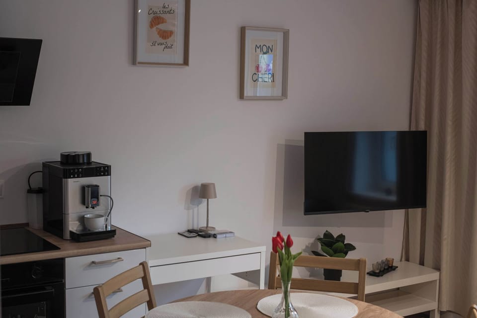 6.	The living room wall is equipped with a flat-screen TV mounted above a white media console, accompanied by a coffee machine and decorative prints.