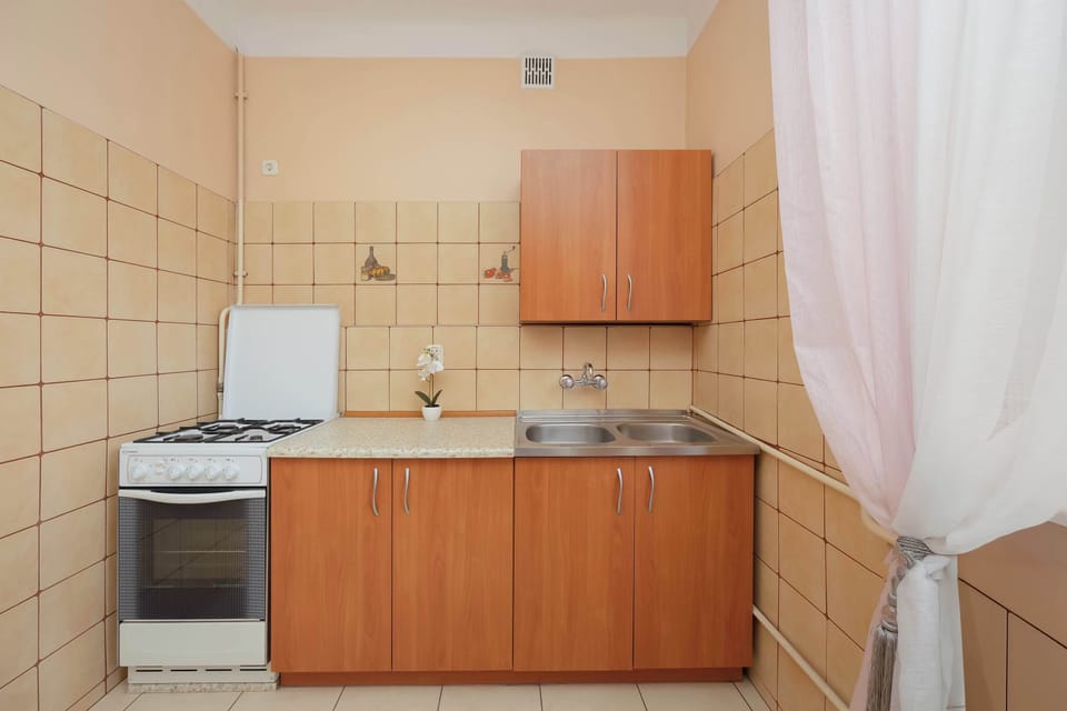 The kitchen featuring wooden cabinets and a stove. Light tiles cover the walls, giving the space a clean appearance. The kitchen looks simple yet fully equipped.