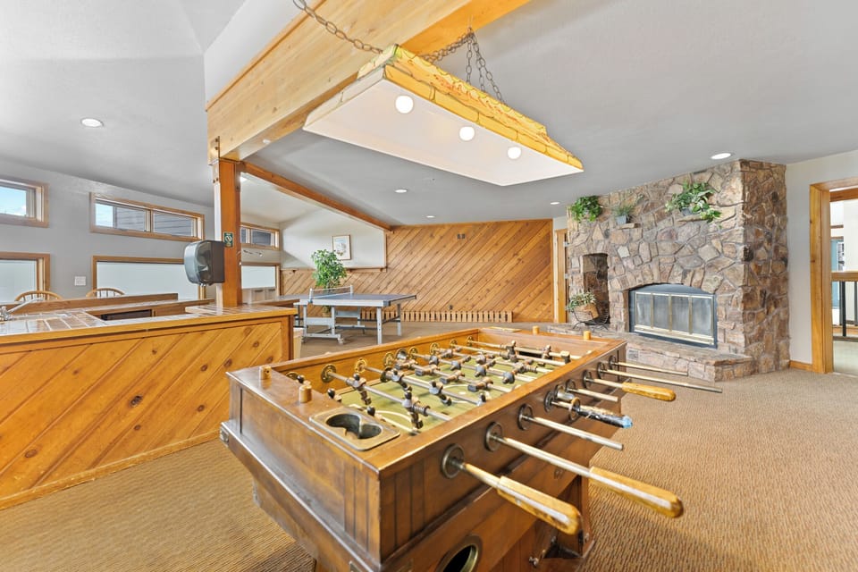 Challenge friends to foosball in your cozy game room, featuring rustic wood details and a stunning stone fireplace for perfect après-ski relaxation.