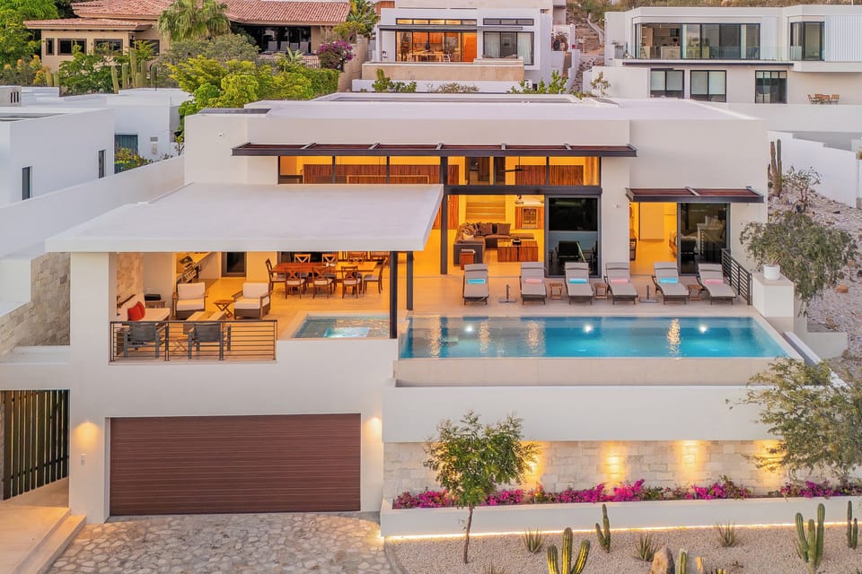 Stunning modern villa showcases contemporary design with terraced levels, infinity pool, and warm evening lighting in an upscale hillside neighborhood.