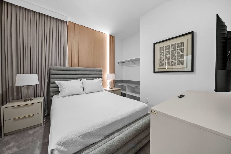 This cozy bedroom features a plush upholstered headboard and crisp, white linens, inviting you to unwind after a day of exploring. The warm wood accents and soft lighting create a tranquil atmosphere, perfect for restful nights.