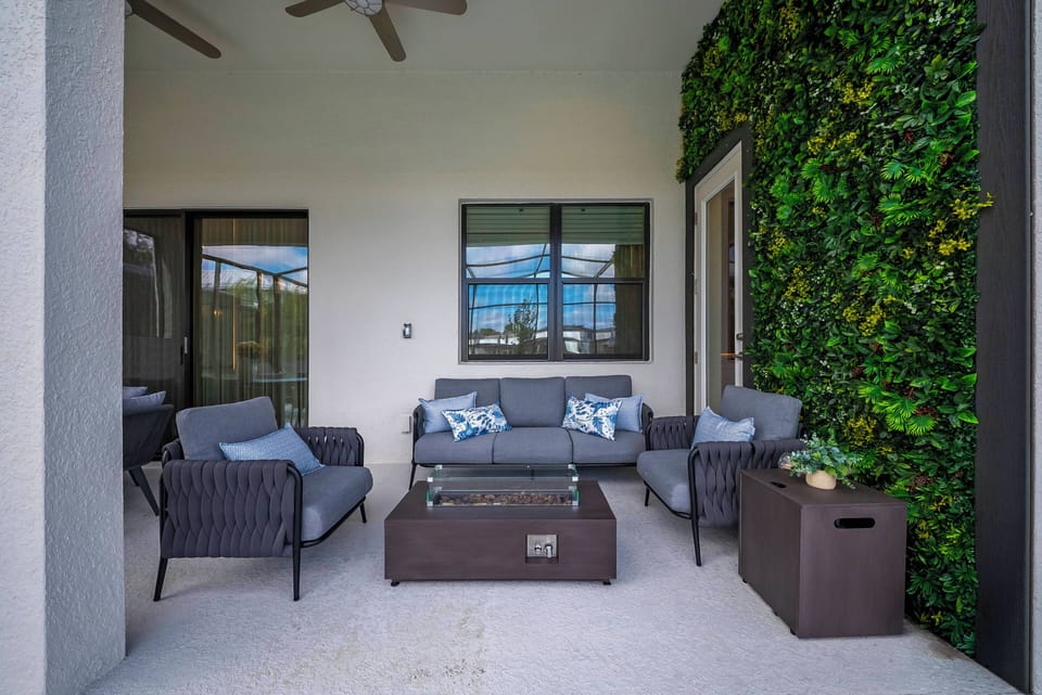 Experience your outdoor retreat amidst lush greenery, where you can unwind on chic gray wicker furniture adorned with colorful throw pillows. Enjoy a refreshing breeze from the ceiling fan as you sip your morning coffee.