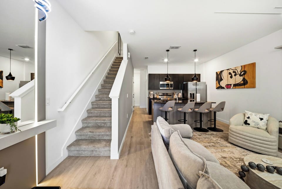 Welcome to a bright living area with large windows and soft, neutral furniture. The modern kitchen features sleek countertops and stylish bar seating for casual meals. After your adventures, relax on the cozy sofa and recharge.