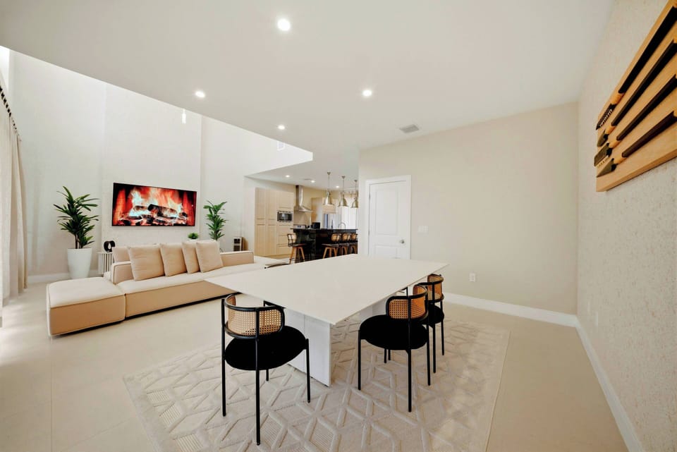 This bright and airy living area boasts a sleek white dining table with stylish black chairs, ideal for gatherings. A plush sectional sofa invites relaxation, enhanced by modern decor and soft lighting for a cozy atmosphere.