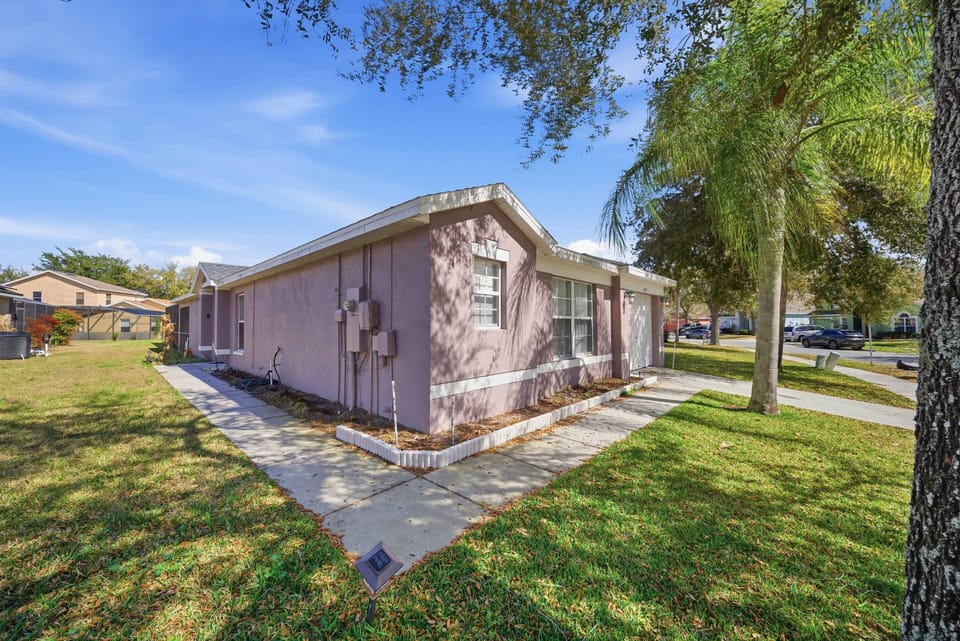Bask in sunlight at this charming pink retreat, where you'll find a well-kept lawn and lush greenery that create an inviting atmosphere, perfect for your relaxation and enjoyment in your home away from home.