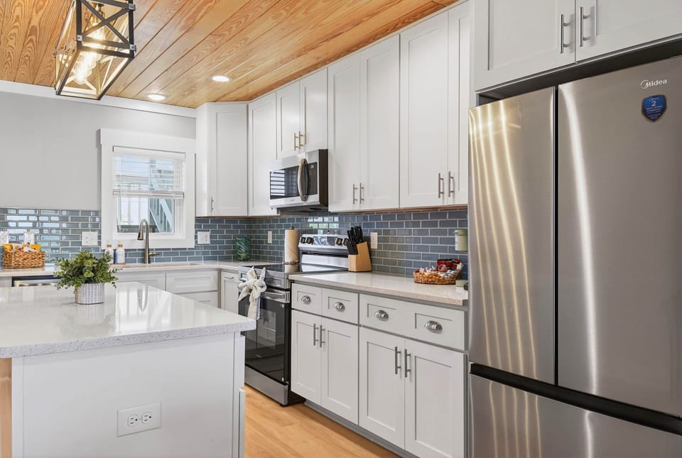 Kitchen with stainless appliances, white shaker cabinets & a pop of teal tiles.