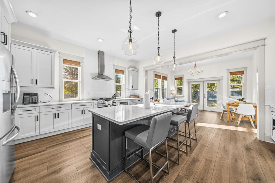 The kitchen island with sleek bar stools, statement pendant lighting, and French doors opening to the back patio — perfect for cooking, entertaining, and indoor-outdoor living in this brand-new Seminole Heights home.