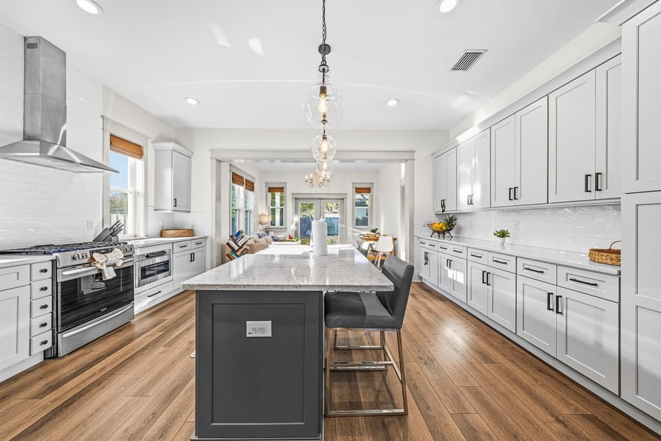 Chef's dream kitchen! Brand-new with floor-to-ceiling white shaker cabinets, a dark center island, elegant pendant lights, stainless steel appliances, and a pro-grade range hood — all on rich hardwood floors.