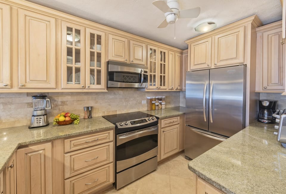 Light wood cabinetry with glass inserts surrounds stainless steel appliances and green granite countertops in the kitchen.