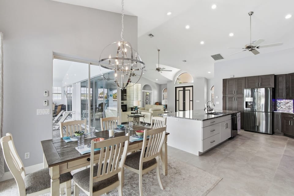 Kitchen and dining area featuring dark cabinetry, stainless refrigerator, granite countertops, and a large decorative chandelier overhead