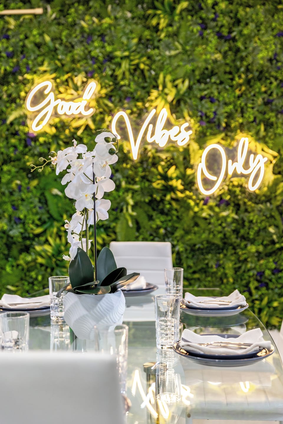Chic dining area with a statement greenery wall and glowing “Good Vibes Only” sign for memorable gatherings.