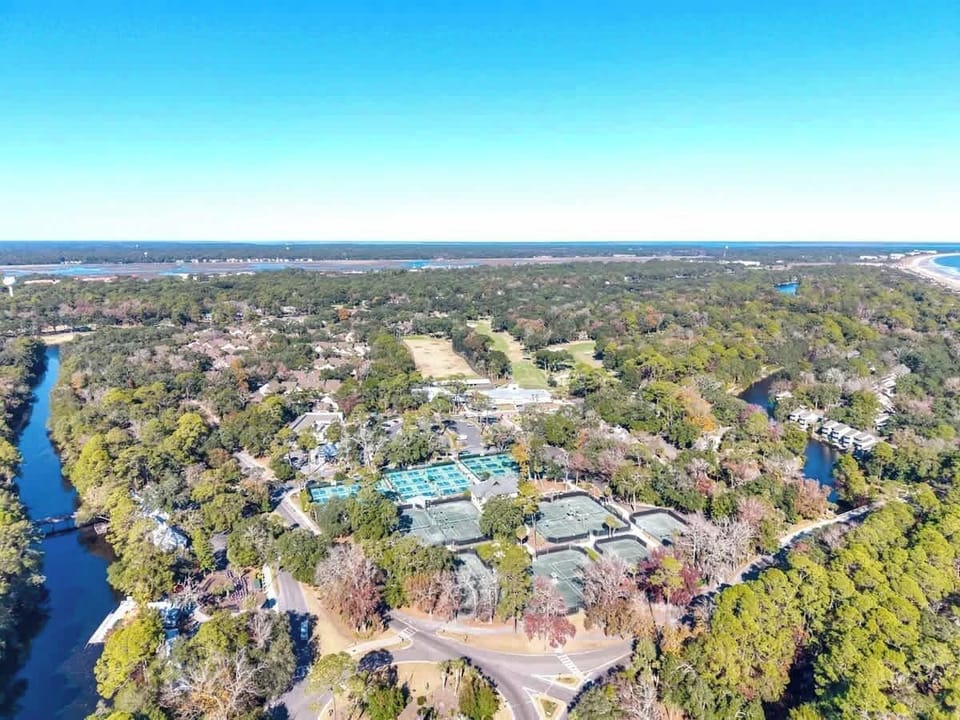 Aerial view of a resort complex nestled among lush trees, with pools and facilities visible near coastal waterways.