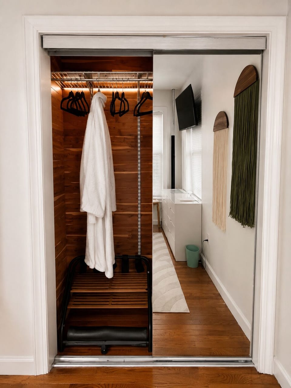 Mirrored closet with warm lighting, hanging space, and luggage rack