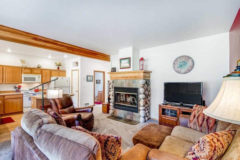 Living room with stone fireplace and kitchen beyond