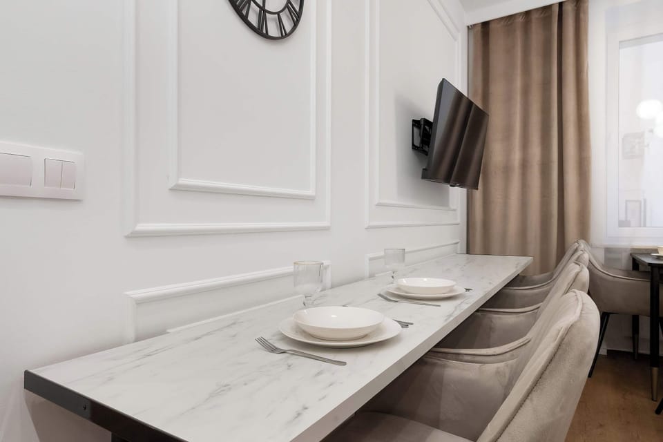 A long, marble-patterned table is accompanied by several grey velvet chairs, offering ample space for larger groups. The room’s white walls and bright lighting enhance the sense of spaciousness.