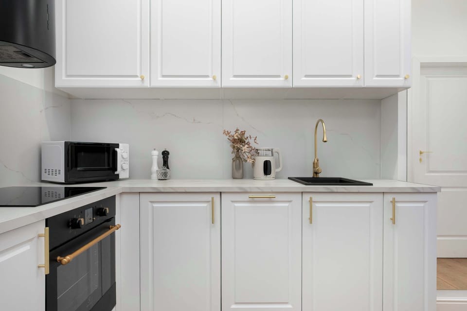 A close-up of the kitchenette reveals a modern microwave placed on the counter next to a sleek black stovetop. The white tiled backsplash and gold faucet add a luxurious feel to the functional workspace.