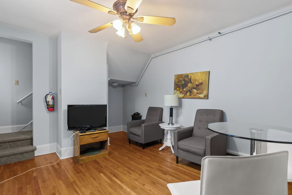 Comfortable living area with armchairs, flat-screen TV, and hardwood floors in a clean, well-lit space.