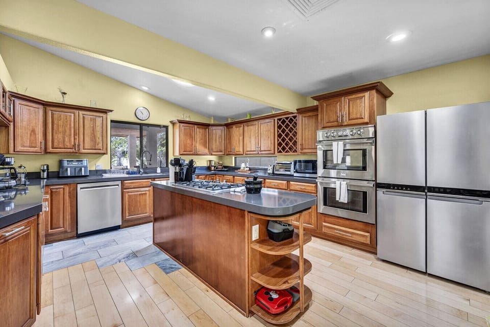 Feed the whole crowd with ease in this stunning, open chef`s kitchen! Featuring an expansive center island with a gas cooktop, double ovens, an extra-large refrigerator, and beautiful wood cabinetry, it is fully stocked with all the modern appliances and 