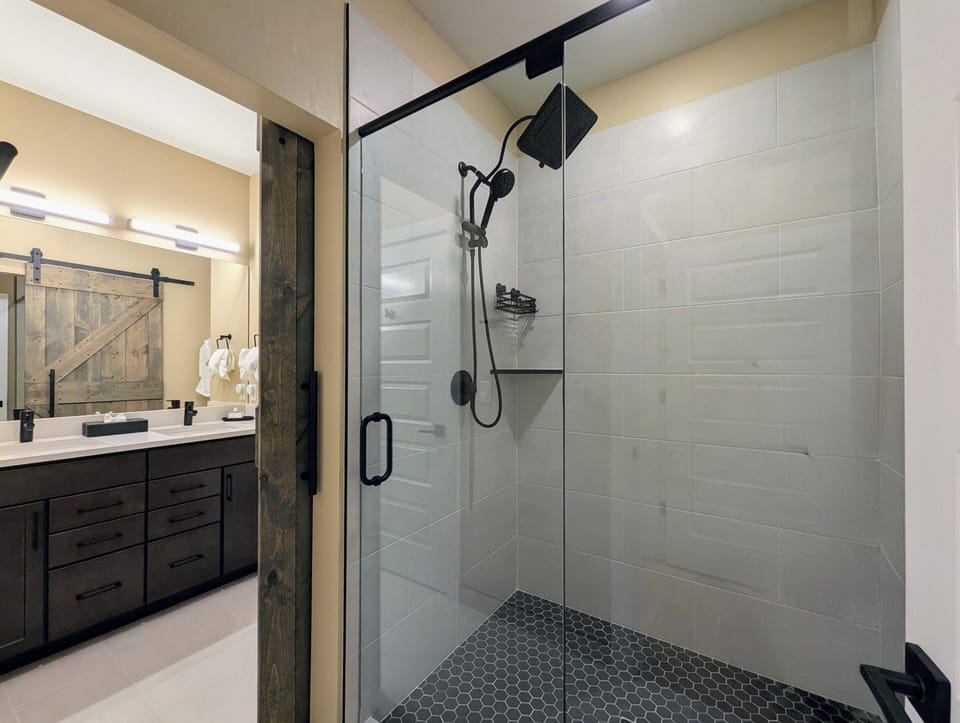 Step into your spa-like ensuite with its spacious glass shower featuring rainfall showerhead and rustic barn door charm.