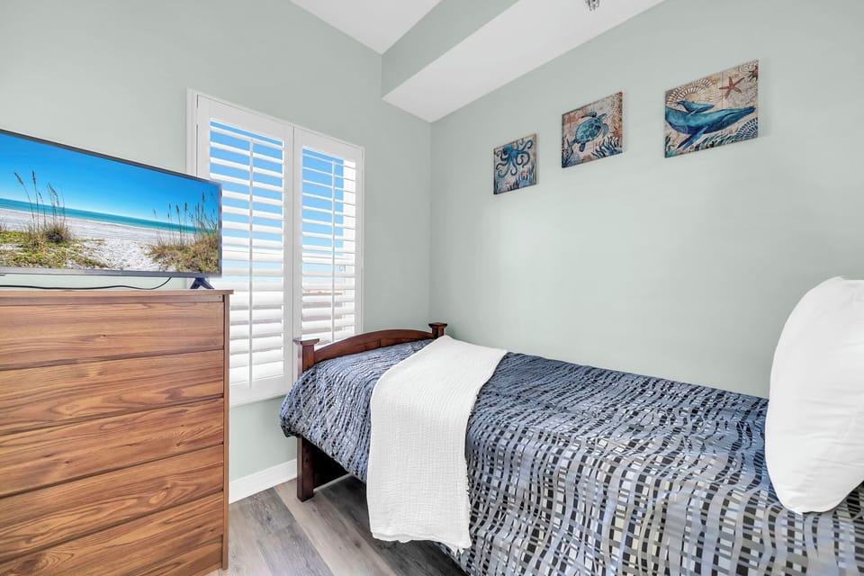 Your cozy bedroom features coastal artwork and natural light streaming through shutters, creating a peaceful retreat.