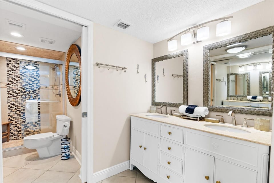 Your spacious bathroom features dual vanities, elegant mirrors, and a stunning mosaic tile shower—perfect for refreshing after beach adventures.