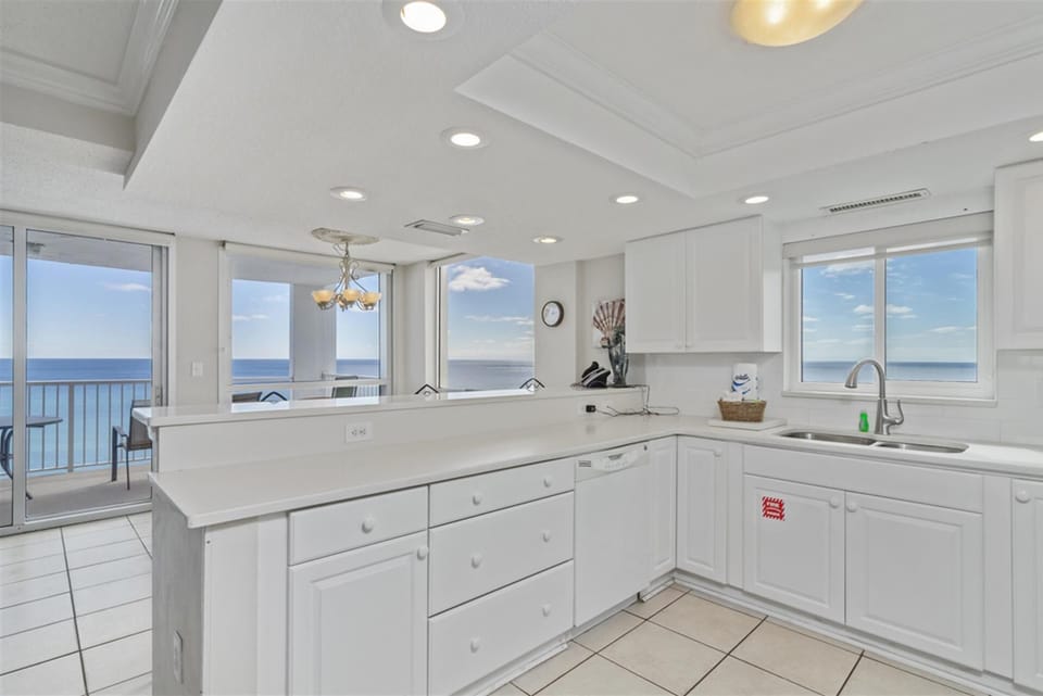 Cook with breathtaking ocean views through floor-to-ceiling windows in your fully equipped kitchen with white cabinetry and modern appliances.