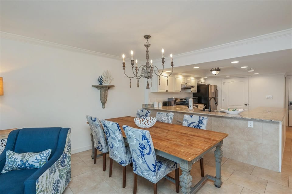 Gather around your coastal dining table for memorable meals beneath an elegant chandelier, with the open kitchen ready for easy meal prep.