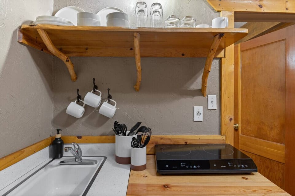 Well equipped kitchenette with open wood shelving, dishes, sink, and cooktop for easy cabin meals.