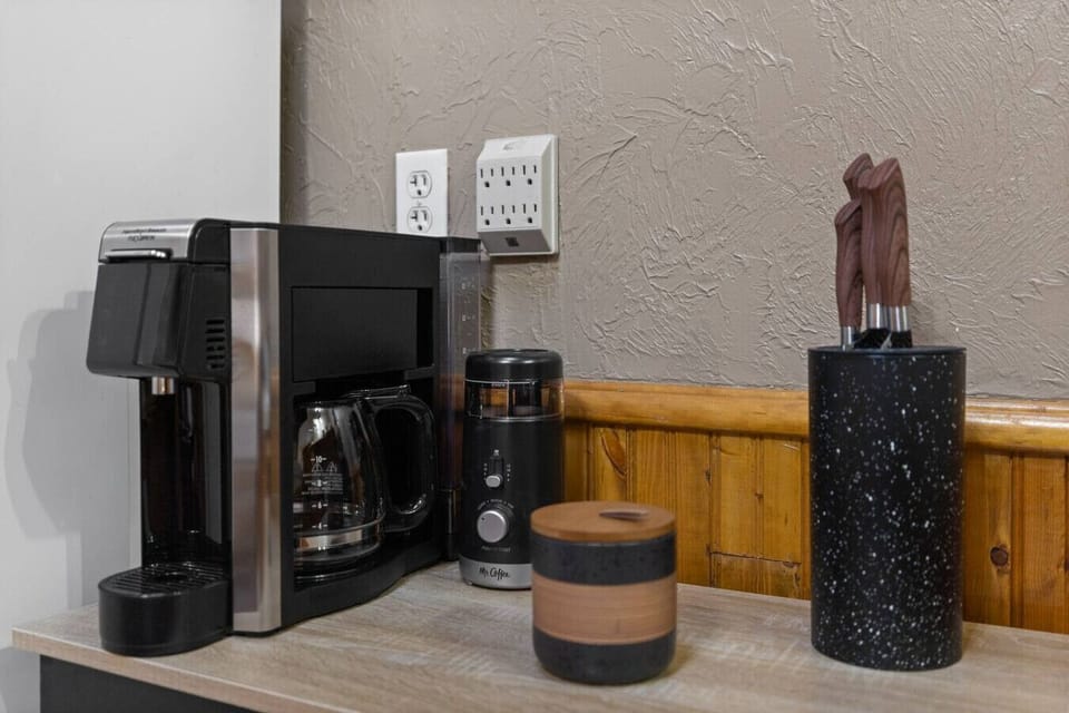 Coffee station with drip coffee maker, grinder, utensils, and mini fridge for convenient mornings.