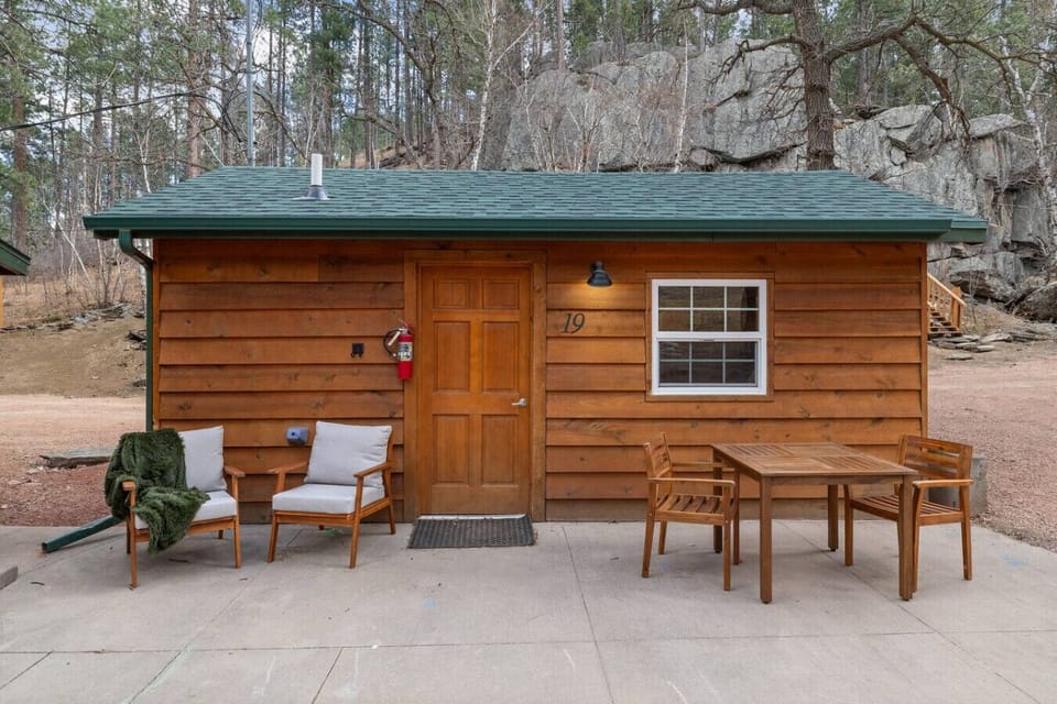 Enjoy your own cabin entrance with outdoor chairs and table, perfect for relaxing in a peaceful forest setting.