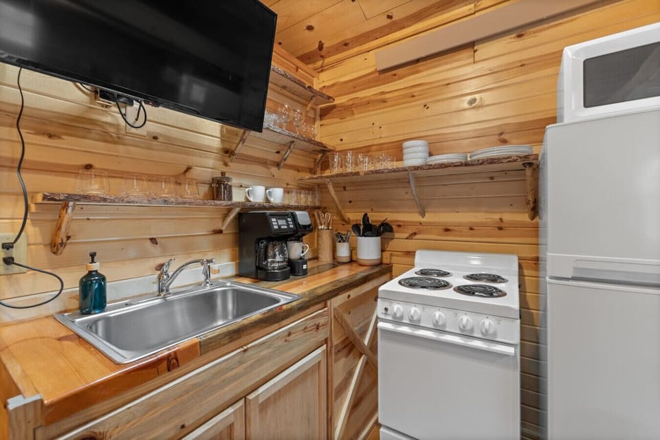 Cook comfortably in the fully equipped kitchen featuring a stove, fridge, microwave, sink, and open shelving with dishware.